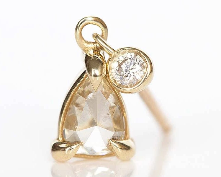 Pear shaped diamond hanging from a single stud earring set in yellow gold