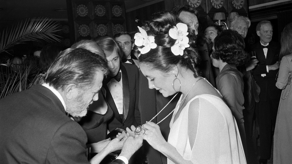 Elizabeth Taylor shows off her Taj Mahal necklace, given to her by husband Richard Burton, featuring a lemon diamond inscribed with Indian love poetry suspended on a gold and ruby chain by Cartier. (Getty Images)