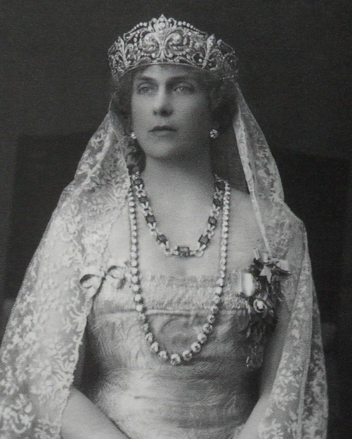 Portrait of Queen Victoria Eugenie wearing the fleurs-de-lis tiara, the chaton necklace, and the earrings, as well as a shorter emerald necklace, c. 1922 (Wikimedia Commons/Public Domain)
