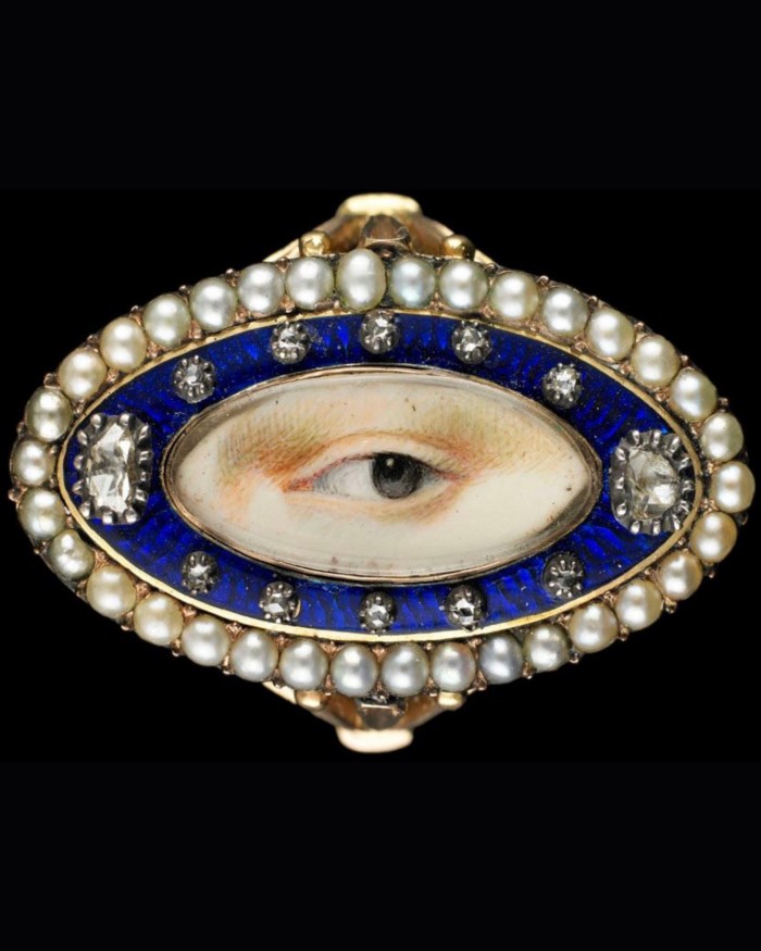 Rose-gold oval Lover's Eye ring surrounded by a blue enamel border containing 10 small and 2 large diamonds enclosed in a border of natural split pearls; brown left eye. Circa 1790.